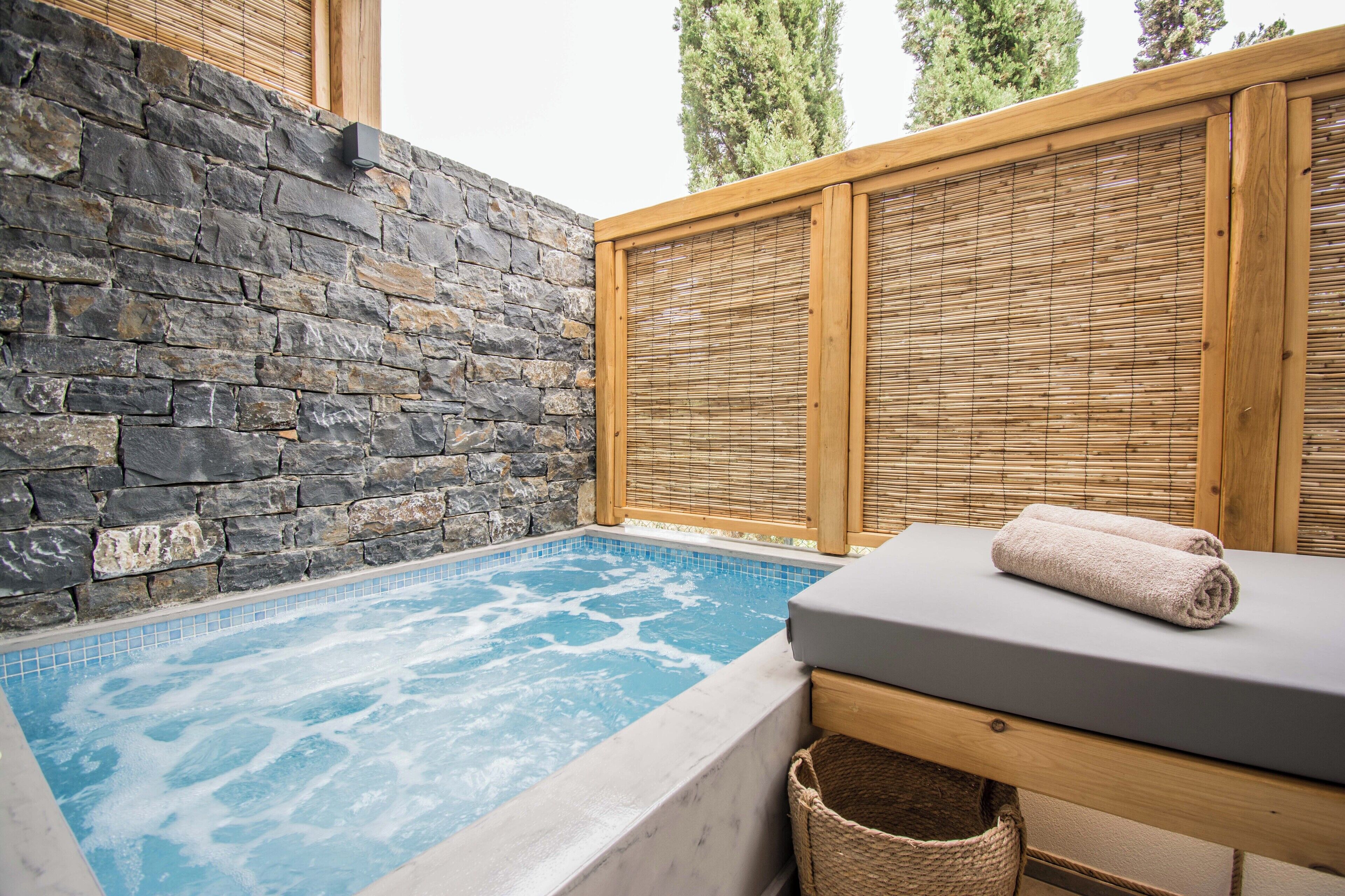 A spa area with a stone wall, wooden paneling, a hot tub, and a massage table with towels.