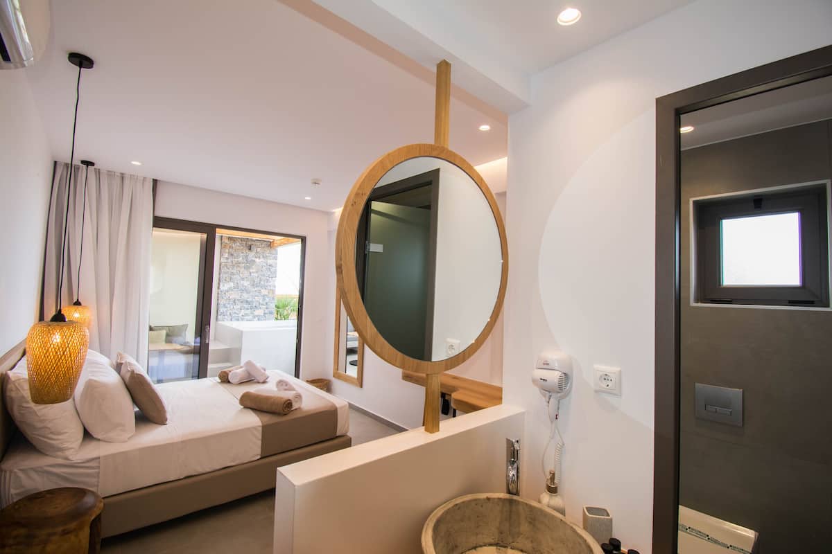 Une chambre moderne avec un grand lit, un miroir rond, une tête de lit en bois et une vue sur un balcon.
