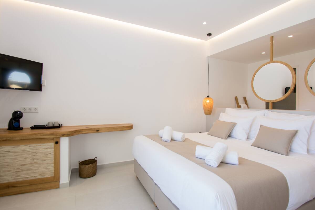 Une chambre d’hôtel moderne dotée d’un bureau en bois, d’un téléviseur à écran plat, d’un lit avec du linge de lit blanc et d’un grand miroir.