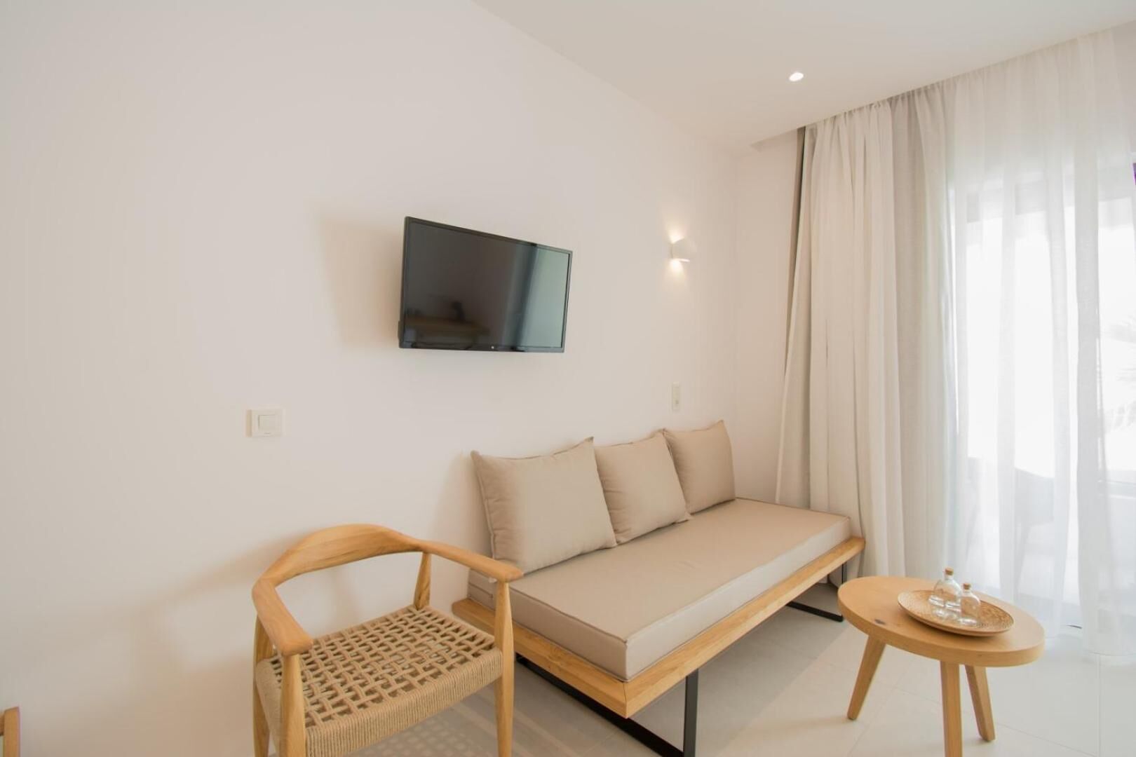 A modern, minimalist room with a sofa, a wooden chair, a small table, and a TV mounted on the wall.