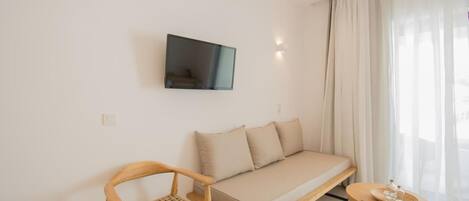 A modern, minimalist room with a sofa, a wooden chair, a small table, and a TV mounted on the wall.
