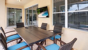 A patio area with a table and chairs, a TV mounted on the wall, and a sliding glass door leading to an indoor space. - 5BR Disney Villa: Pool & Spa, Game Room, Theater (Kissimmee)