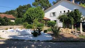 A white house with a garden, a boat in the driveway, and a fence.