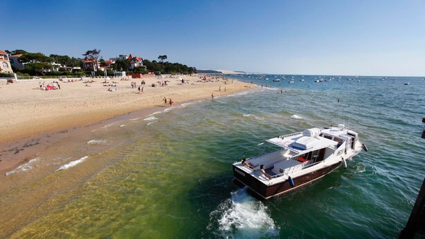 A boat on a clear day near a sandy beach with buildings in the background.
