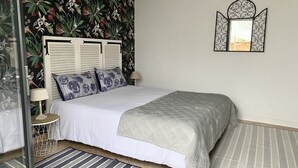 A bedroom with a bed, a nightstand, a lamp, a mirror, and a floral wallpaper.