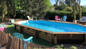 A wooden pool surrounded by colorful Adirondack chairs, with a wooden deck and lush greenery in the background.
