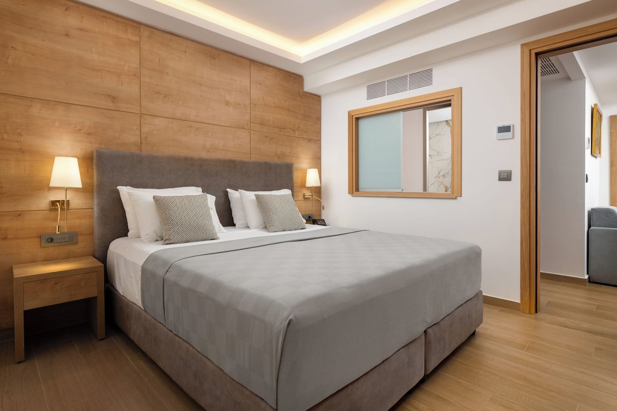 A modern hotel room with a large bed, wooden headboard, bedside lamps, and a large mirror.