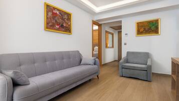 Una sala de estar moderna con un sofá y un sillón grises, piso de madera y dos cuadros enmarcados en las paredes.
