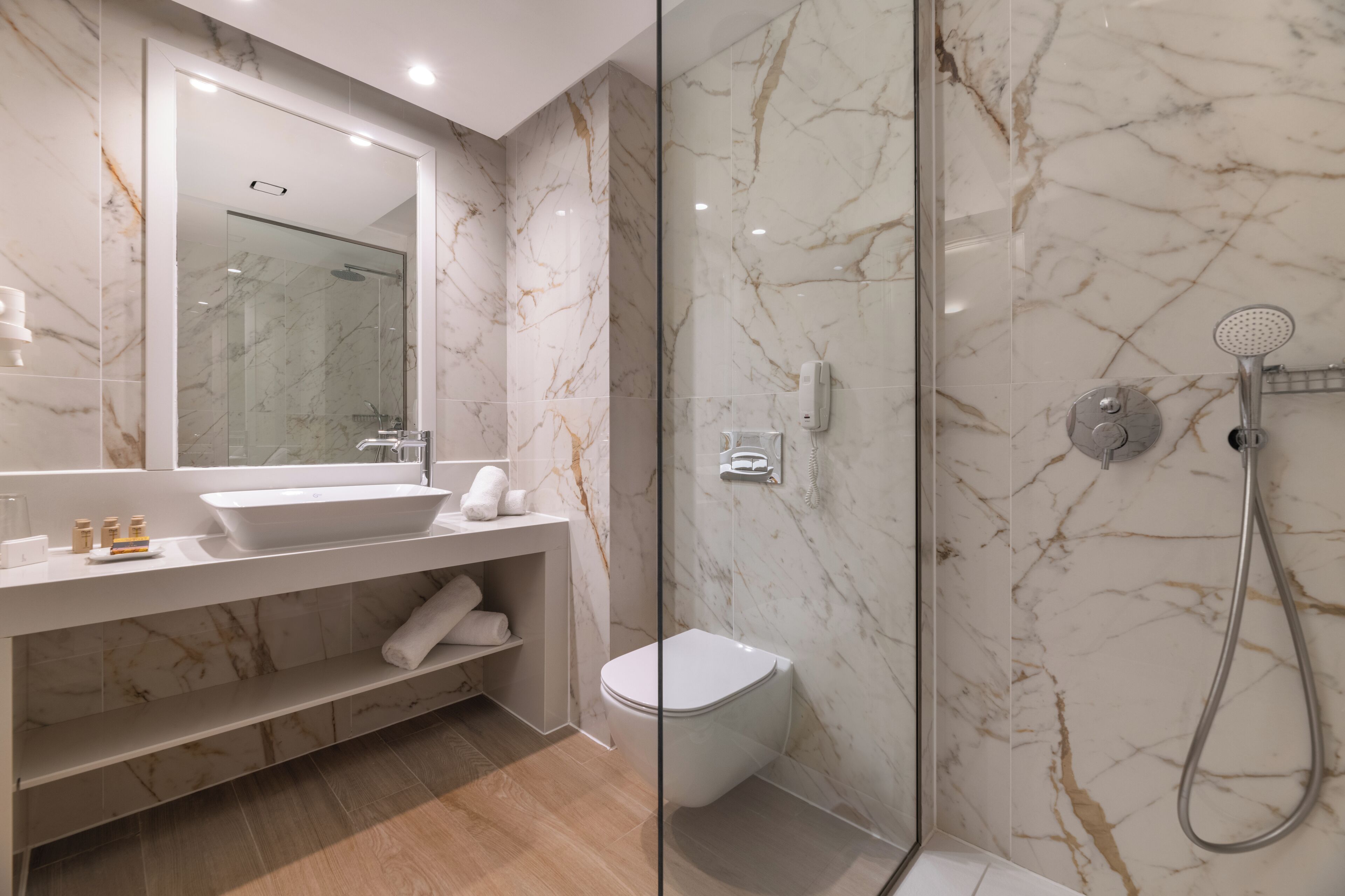 Een moderne badkamer met een douche in een glazen cabine, een witte wastafel en een wand betegeld met marmer.