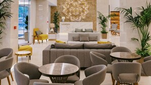 A modern hotel lobby with a reception desk, seating area, and decorative wall art. - Hotel Acandia (Rhodes)