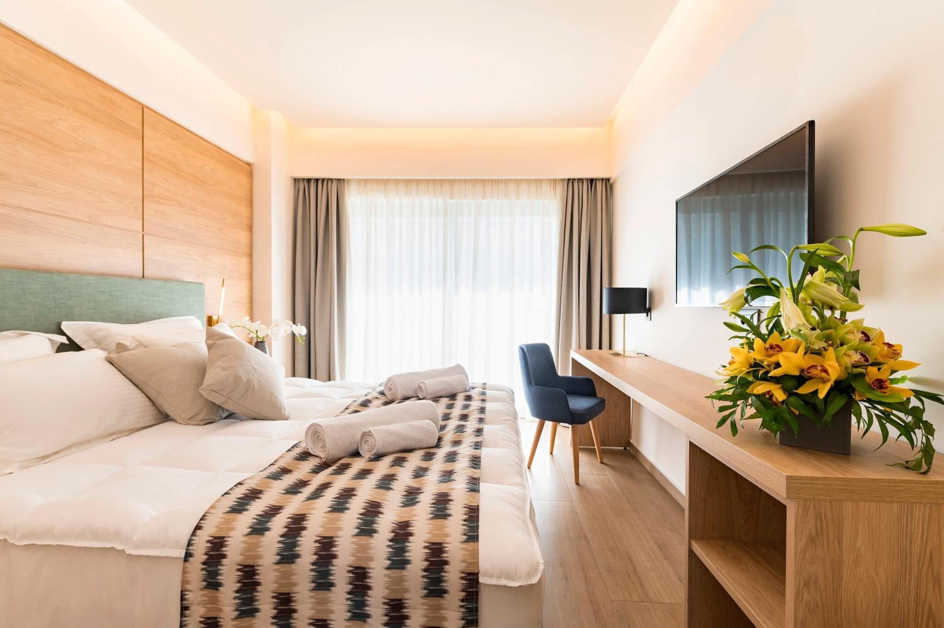 A hotel room with a bed, a desk, a chair, a TV, and a flower arrangement.