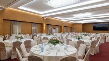 Un salón de banquetes con mesas redondas dispuestas para eventos, equipado con botellas de agua, vasos y centros de mesa florales.