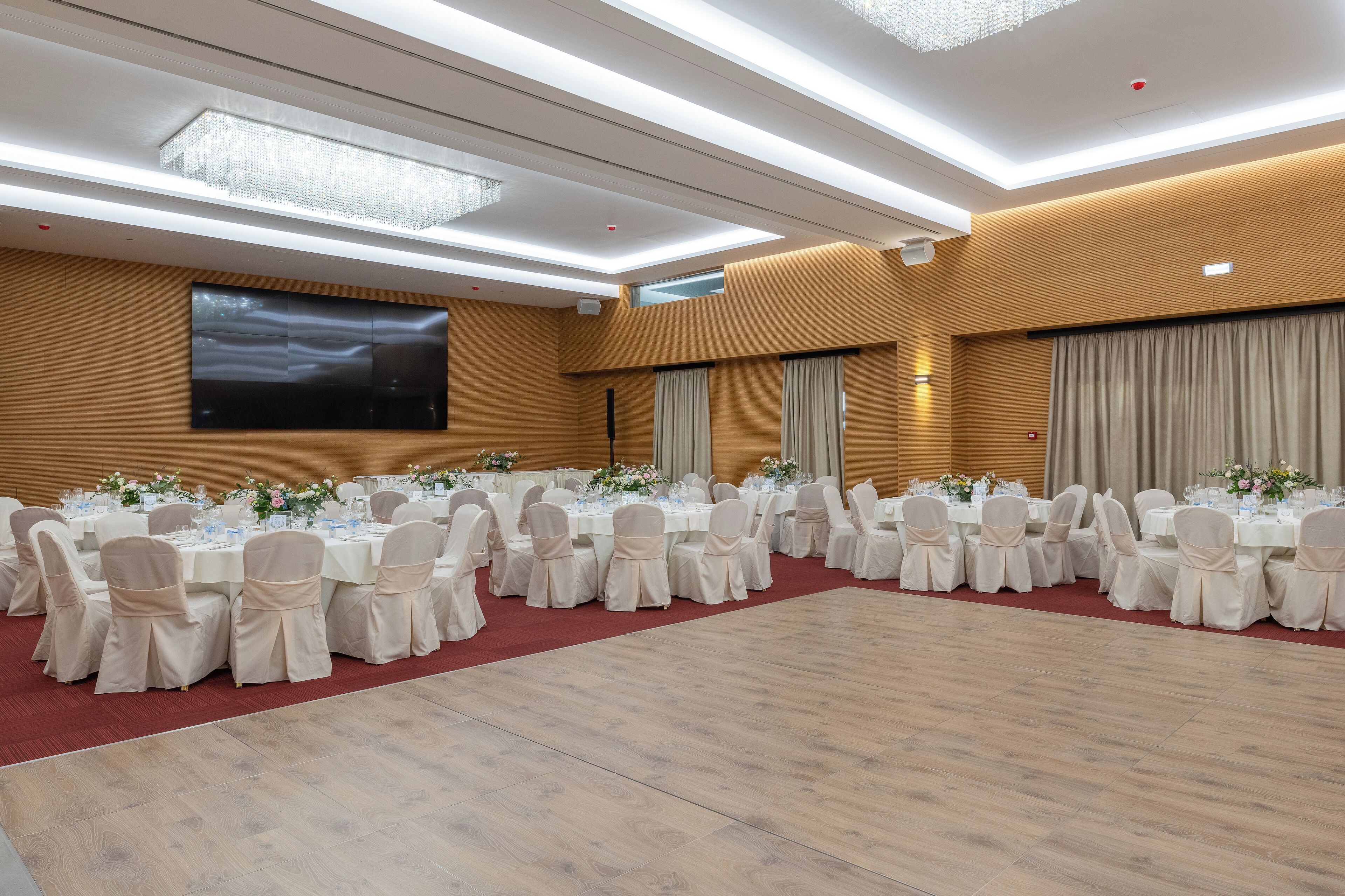 A banquet hall with round tables, white chairs, and a large screen on the wall.