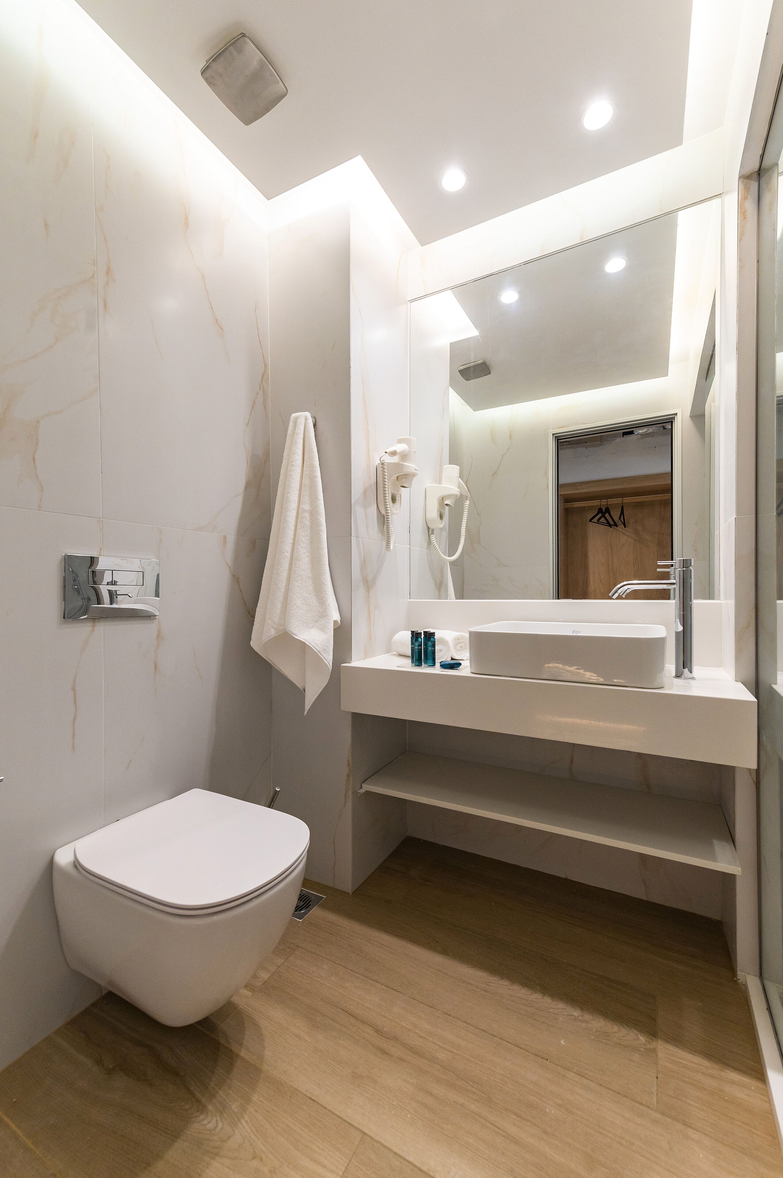Ein modernes Badezimmer mit Toilette, Marmorwänden, einem großen Spiegel und Holzboden.