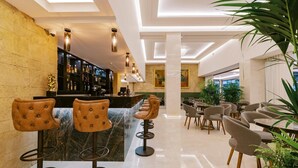 A modern bar area with leather barstools, a marble counter, and a well-lit interior with ceiling lights and a large plant. - Hotel Acandia (Rhodes)