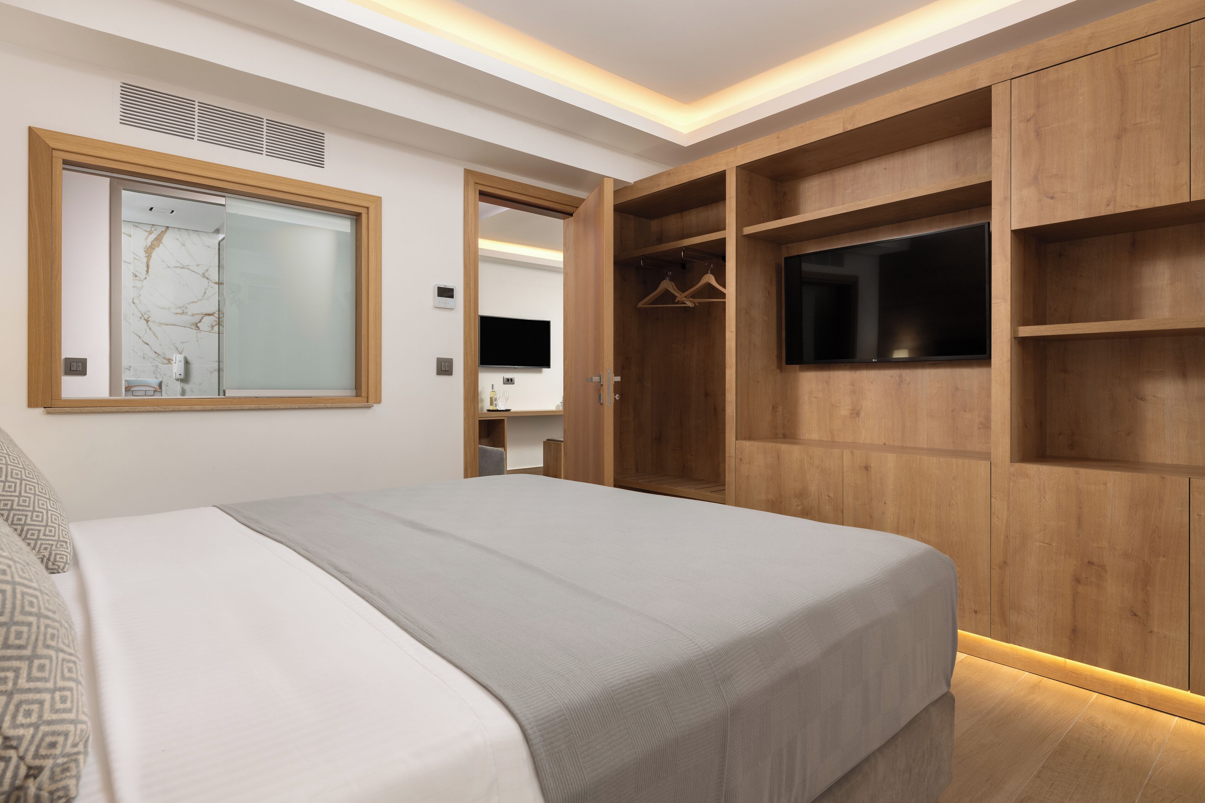A bedroom with a bed, a wardrobe, a mirror, and a television.
