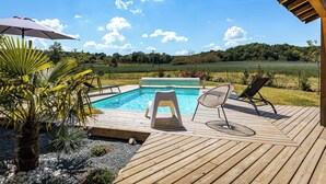 A wooden deck with a pool, two chairs, and a palm plant. - holiday home with private pool and large covered terrace. (La Bachellerie)