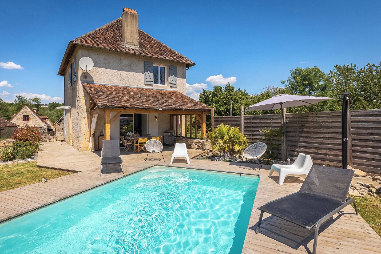 Una casa con piscina, area relax all'aperto e terrazza in legno.