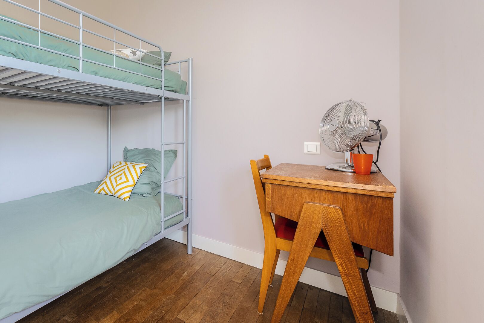 Una cama litera con ropa de cama verde, un escritorio de madera con un ventilador y una silla.