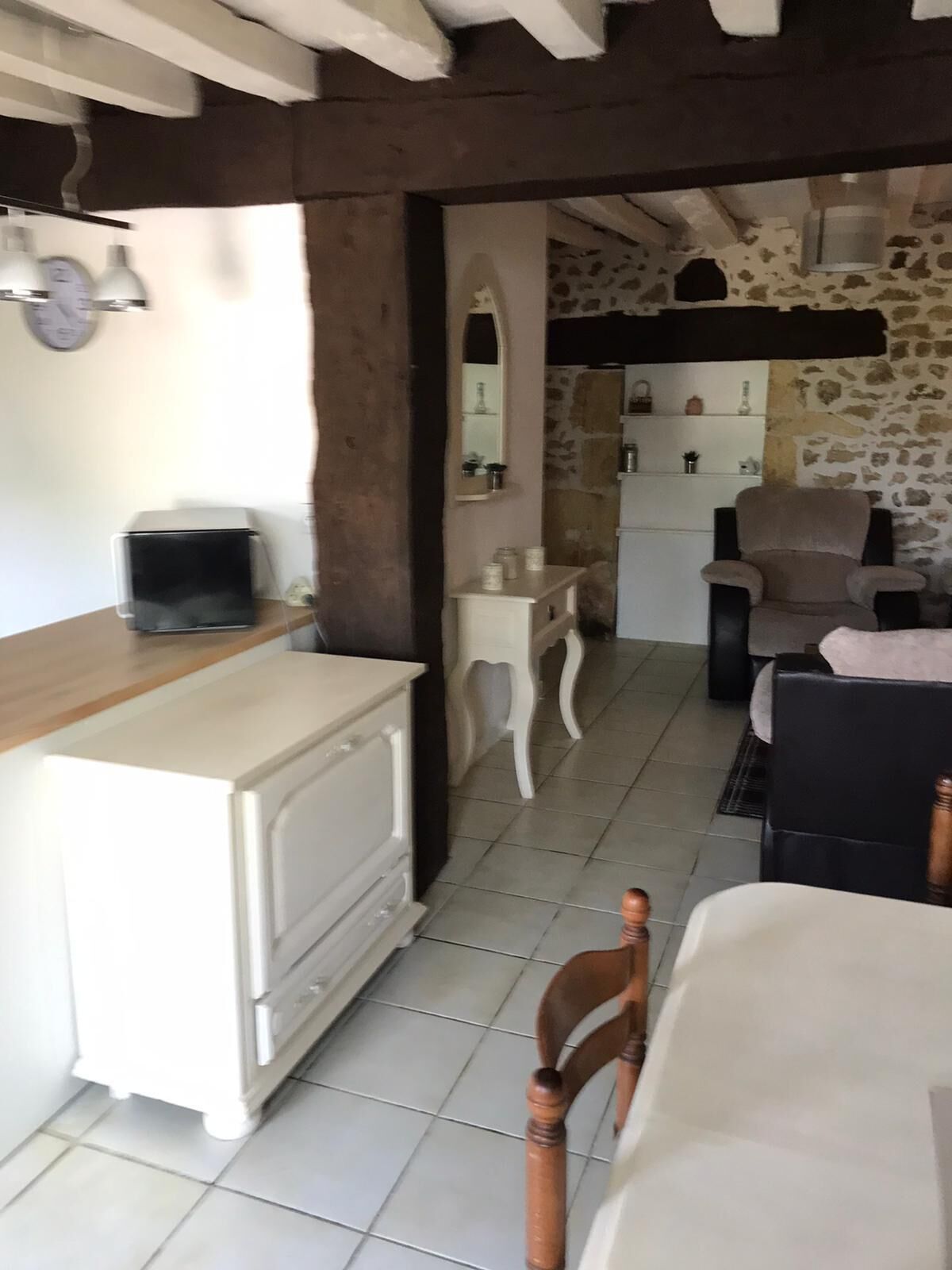 A cozy room with a white dresser, a wooden chair, a stone wall, and a small table with a lamp.