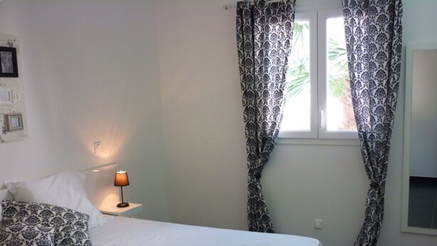 Una camera da letto con un letto, un comodino con una lampada, tende a motivi decorativi e una finestra.