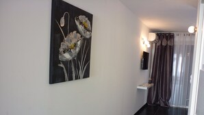 Un corridoio con un dipinto floreale bianco e nero appeso alla parete, un lampadario e un pavimento scuro.