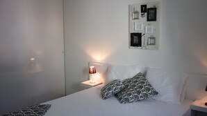 Un dormitorio con una cama, una mesita de noche con lámpara y una pared decorada con marcos de fotos.