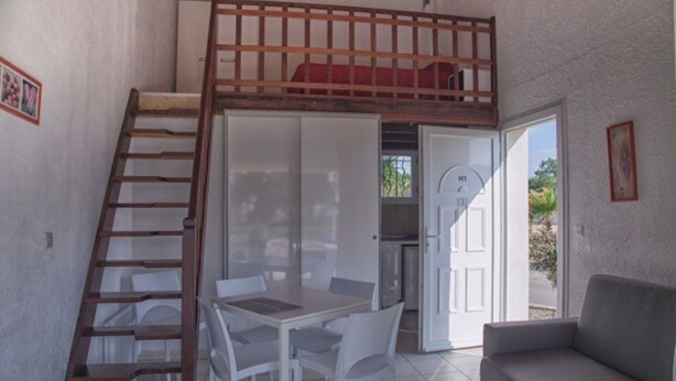 Un espacio tipo loft con una escalera de madera, una zona de comedor con mesa y sillas, y un sofá.