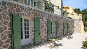 Un edificio de piedra con contraventanas verdes y mesas al aire libre.