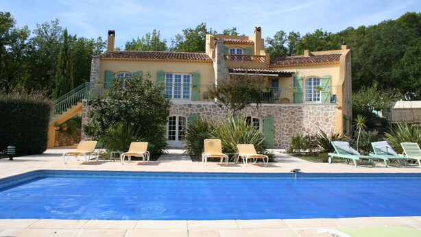 Un edificio de dos pisos con piscina, mobiliario exterior y fachada de piedra.