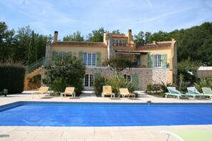 A two-story building with a swimming pool, outdoor seating, and a stone facade. - Le Mas des Tarentes, nestled among vineyards and forests (Trans-en-Provence)