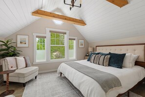 Un dormitorio con una cama grande, una ventana, una planta y una viga de techo de madera.
