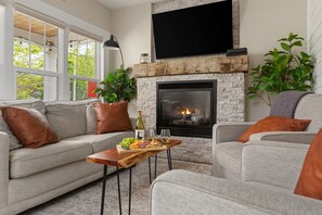 Una sala de estar con chimenea, un sofá, una mesa de centro con bocadillos y bebidas, y un televisor montado sobre la chimenea.