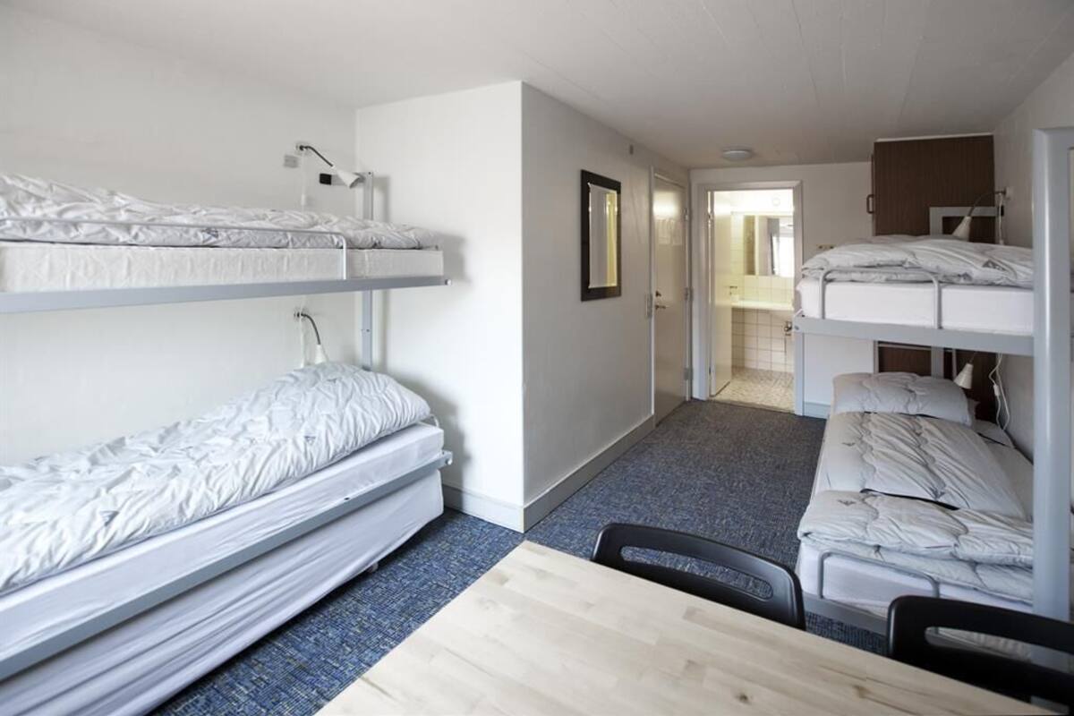 A dormitory room with bunk beds, a desk, and a chair.
