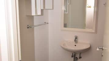 Un baño pequeño y limpio con inodoro, lavamanos y espejo. Hay un perchero y una planta en maceta en la pared.