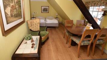 A cozy room with a bed, a dining table with chairs, a green armchair, and a small table with a plant.