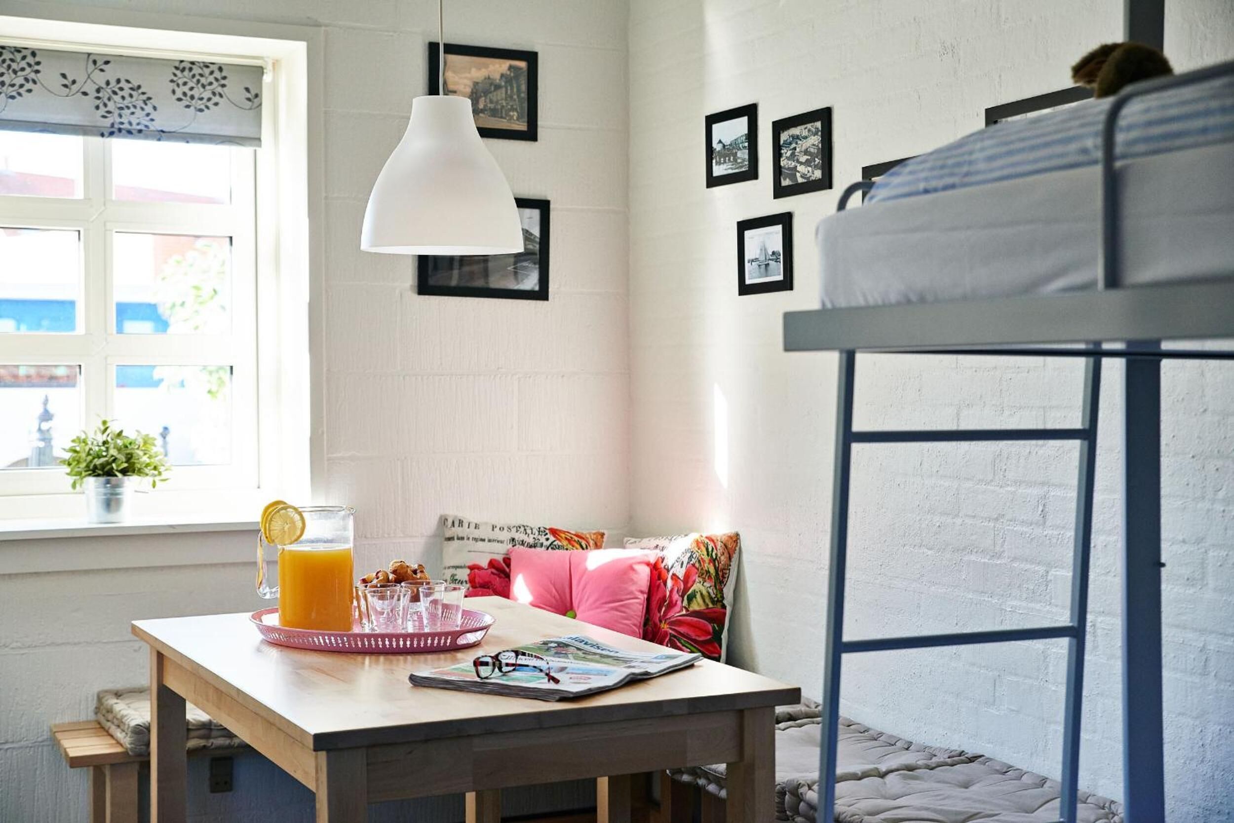 Una habitación con literas, una mesa con cosas para el desayuno, una ventana con vistas y cuadros en la pared.