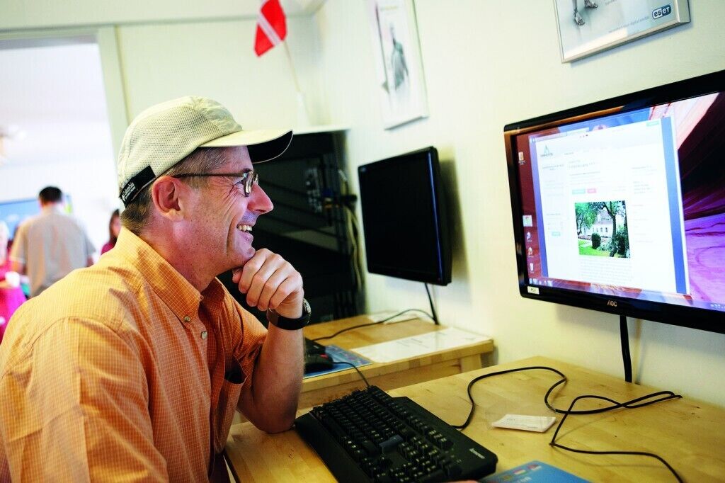 Un hombre sentado en un escritorio con un monitor de computadora mostrando una página web.