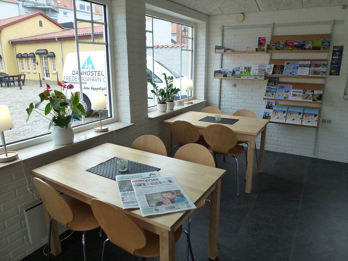 A cozy cafe with wooden tables and chairs, a window with a view of the street, and a wall with postcards and books.