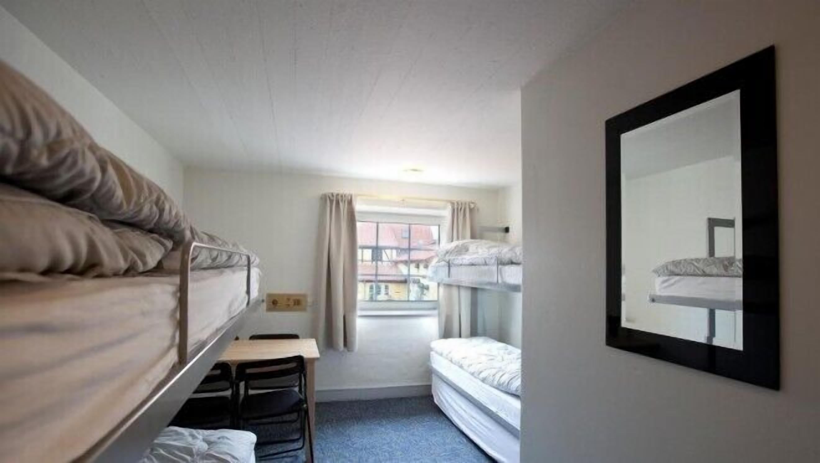 A small, compact room with two bunk beds, a desk, and a mirror on the wall.