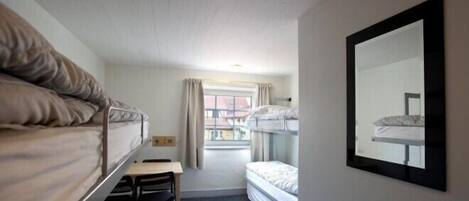 A small, compact room with two bunk beds, a desk, and a mirror on the wall.
