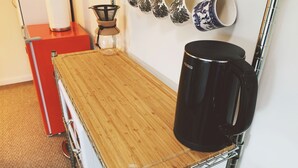 En köksbänk med en kaffebryggare, en vattenkokare och en kaffekanna. Flera muggar hänger på väggen.