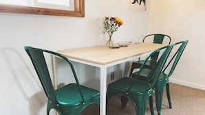 Ett matbord med fyra gröna stolar, en vas med blommor och en inramad tavla på väggen.