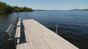 En träbrygga som sträcker sig ut i en stilla sjö, med svanar i fjärran och en skogbeklädd strand.