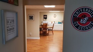 A hallway leading to a dining area with wooden flooring, a table, and chairs. A framed inspirational quote is on the wall, and a university logo is visible. - Spacious suite with fenced back yard, deck, gas grill, fireplaces and splash pad (Athens)