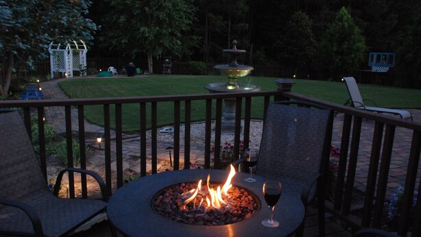 An outdoor patio with a round table, two chairs, a fire pit, and a fountain. - Spacious suite with fenced back yard, deck, gas grill, fireplaces and splash pad (Athens)