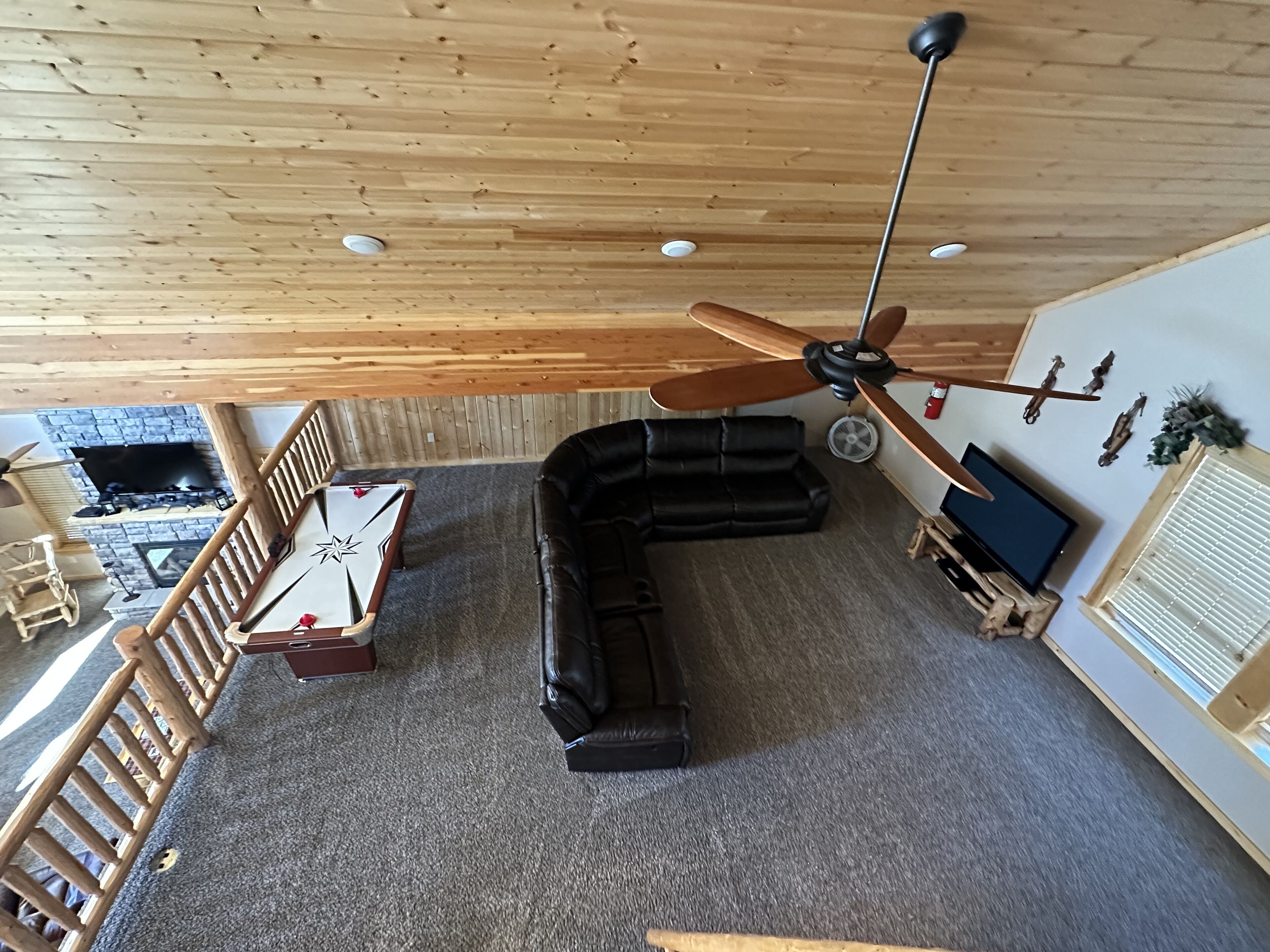 A spacious living area with a black leather sofa, a wooden ceiling, and a ceiling fan.