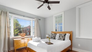 Une chambre à coucher avec un lit en bois, une table de chevet, une fenêtre avec des rideaux et un ventilateur de plafond.