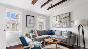 A living room with a grey sofa, a blue chair, a round coffee table, and a large abstract painting. - Casa Bella Suite B | 3 Blocks to King Street (Charleston)