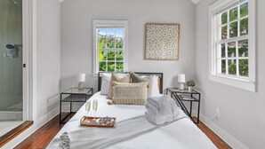 A bedroom with a bed, two bedside tables, a window, and a shower area. - Casa Bella Suite B | 3 Blocks to King Street (Charleston)